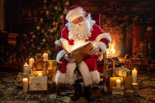 © Photowerkstatt Henrik Matzen – Weihnachtsmann Claudius Weihnachtsmann Claudius im Thronsessel mit Goldenem Buch, Kerzen und Geschenken im Kaminzimmer nebst Kerzen